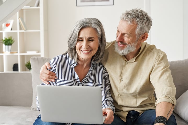 Middle aged couple sat using laptop and smiling